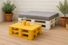 Outdoor seating area with a yellow pallet coffee table and a white pallet bench with a gray cushion. Anteprima dell’immagine prodotto