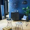 A stylish living room with blue walls, featuring a large mirror, a cabinet, a chair, plants, and a floor cushion. Náhled obrázku produktu