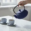 A hand pours tea from a blue teapot into a gray cup. Podgląd zdjęcia produktu