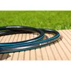A black garden hose with blue stripes lies coiled on a wooden deck, with green grass in the background. Voir les images du produit