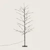 A decorative LED tree with a black trunk and branches, illuminated by small white lights, standing on a black square base with a black power cord extending to the left. Náhled obrázku produktu