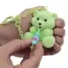 A hand holding a small green teddy bear toy with a chain around its neck and a small blue bottle with pink accents in its paws. Anteprima dell’immagine prodotto