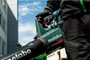 A person wearing black clothing and gloves is holding a Metabo leaf blower outdoors. Produktbild-Vorschau
