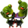 Two green ceramic frogs with orange eyes are sitting together, holding a purple leaf. Produktbild-Vorschau