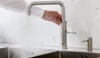 A person's hand is shown turning on a modern kitchen faucet over a sink. Anteprima dell’immagine prodotto
