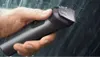 A hand holding a black and silver electric trimmer with water droplets on it, suggesting it is being used in a shower or wet environment. Anteprima dell’immagine prodotto