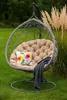A hanging egg chair with a cushion and blanket sits on a grassy lawn next to tall ornamental grass. Produktbild-Vorschau