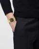 A person wearing a black sweater and black pants, with a gold watch on their left wrist. Náhled obrázku produktu