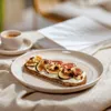 A breakfast setting with a slice of toast topped with cream cheese, figs, and nuts, next to a cup of espresso. Produktbild-Vorschau