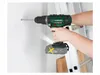 A person is using a cordless drill to make a hole in a white wall, with a ladder in the background. Podgląd zdjęcia produktu