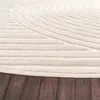 A close-up view of a cream-colored rug with a geometric pattern, placed on a dark wooden floor. Voir les images du produit