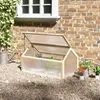 A wooden cold frame greenhouse with a clear lid is placed on gravel next to a brick wall and a window. Voir les images du produit