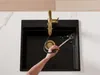 A person is using a gold faucet with a pull-out spray in a black kitchen sink. Produktbild-Vorschau