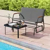 A two-seater glider bench and a small side table are placed on a patio next to a swimming pool, with lush green foliage in the background. Anteprima dell’immagine prodotto