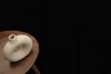 A beige donut-shaped vase sits on a wooden table against a black background. Voir les images du produit