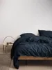 A close-up view of a bed with dark blue linen bedding. Produktbild-Vorschau