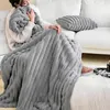 A person is sitting on a couch wrapped in a thick, textured gray blanket. Produktbild-Vorschau