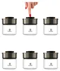 A hand is pressing the lid of one of six identical glass storage jars arranged in two rows. Produktbild-Vorschau