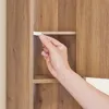 A hand is inserting a white shelf support into a wooden cabinet. Náhled obrázku produktu