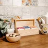 A wooden tea box with tea bags, a bowl of chocolates, and a teacup on a wooden counter, with a tiled backsplash. Podgląd zdjęcia produktu