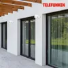 Two white outdoor wall lights are mounted on a white wall next to large glass windows. Wooden beams are visible overhead. Produktbild-Vorschau