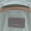 A close-up view of a light green baby carrier, showing a zipper and a gray label with text. Náhled obrázku produktu