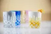 A collection of colorful crystal glasses with a diamond cut pattern, one of which is filled with a beverage and garnished with an orange peel. Produktbild-Vorschau