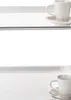 Two white coffee cups and saucers are displayed on white surfaces, separated by a white space. Voir les images du produit