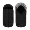 Two black baby footmuffs are shown side-by-side against a white background. The footmuff on the left is closed, while the one on the right is open, revealing a grey fur lining around the hood and a black interior. Both footmuffs have a quilted design and z Náhled obrázku produktu