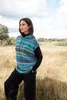 A woman stands in a field wearing a knitted poncho. Produktbild-Vorschau