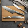 Three kitchen knives are arranged on a wooden cutting board, with some mushrooms scattered around the board. Produktbild-Vorschau