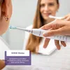 A woman is reflected in a mirror, holding an electric toothbrush and demonstrating its use. Produktbild-Vorschau