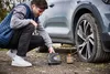 A man is using a portable tire inflator next to a car. Produktbild-Vorschau