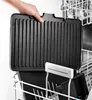 A hand is holding a black grill plate over a dishwasher rack. Podgląd zdjęcia produktu