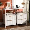 Two white nightstands are shown in a bedroom setting, with decorative items and electronics on top and within. Náhled obrázku produktu
