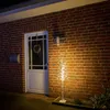 A decorative LED tree with neutral white lights stands on a walkway in front of a brick house entrance at night. Produktbild-Vorschau