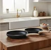 Two frying pans are placed on a wooden cutting board in a kitchen setting, with a sink and faucet in the background. Náhľad obrázku produktu