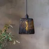 A black rattan-look pendant light hangs against a textured wall, with a plant in the foreground. Produktbild-Vorschau