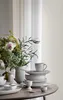 A stack of plates and a cup are arranged on a table next to a vase of flowers. Produktbild-Vorschau