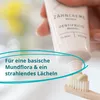 A hand holding a tube of toothpaste, squeezing it onto a toothbrush. Produktbild-Vorschau
