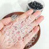 A hand holding a pile of small, transparent hair ties, with a jar of black hair ties in the background. Anteprima dell’immagine prodotto