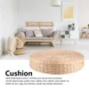 A round woven cushion is placed in the foreground of a living room setting with a sofa and furniture in the background. Voir les images du produit