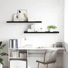 A clean, minimalist shot of two black floating shelves mounted on a white wall, displaying various decorative items and books. Náhled obrázku produktu