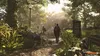 Two people walking on a path in a park with lush greenery and sunlight filtering through the trees. Produktbild-Vorschau