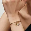 A close-up shot of a person's arm wearing a gold Pandora bracelet with two heart-shaped charms. Produktbild-Vorschau
