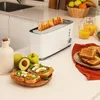 A kitchen counter scene with a toaster, toast, avocado toast, fruit, and juice. Voir les images du produit