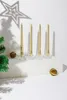 Four gold spiral candles on clear holders on a white surface, with a Christmas tree branch and decorative balls. Anteprima dell’immagine prodotto