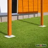 Two wooden posts with metal bases are shown on a green lawn in front of a building with an orange wooden wall. Produktbild-Vorschau