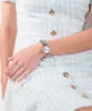A close-up shot of a woman's wrist wearing a silver watch. Produktbild-Vorschau
