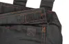 A close-up view of black overalls with orange stitching and velcro fasteners. Produktbild-Vorschau